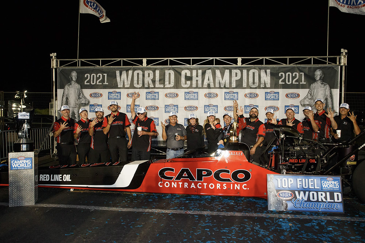 Steve Torrence and team stand in front of a background that says 2021 World Champion. They all wear red and black outfits. 