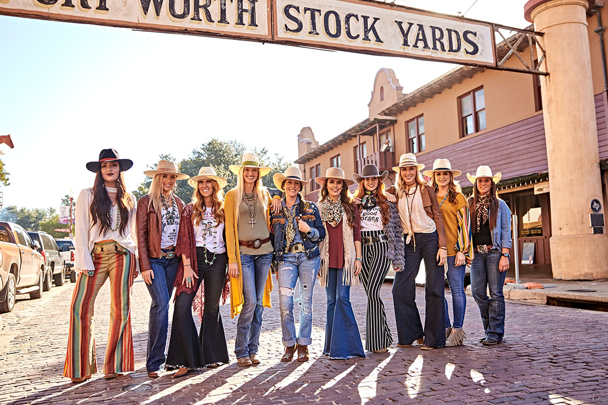 A group of women stand under the Fort Worth Stock Yards sign. They are decked head to toe in Western wear, and they are all wearing a fashion hat from American Hat Company.
